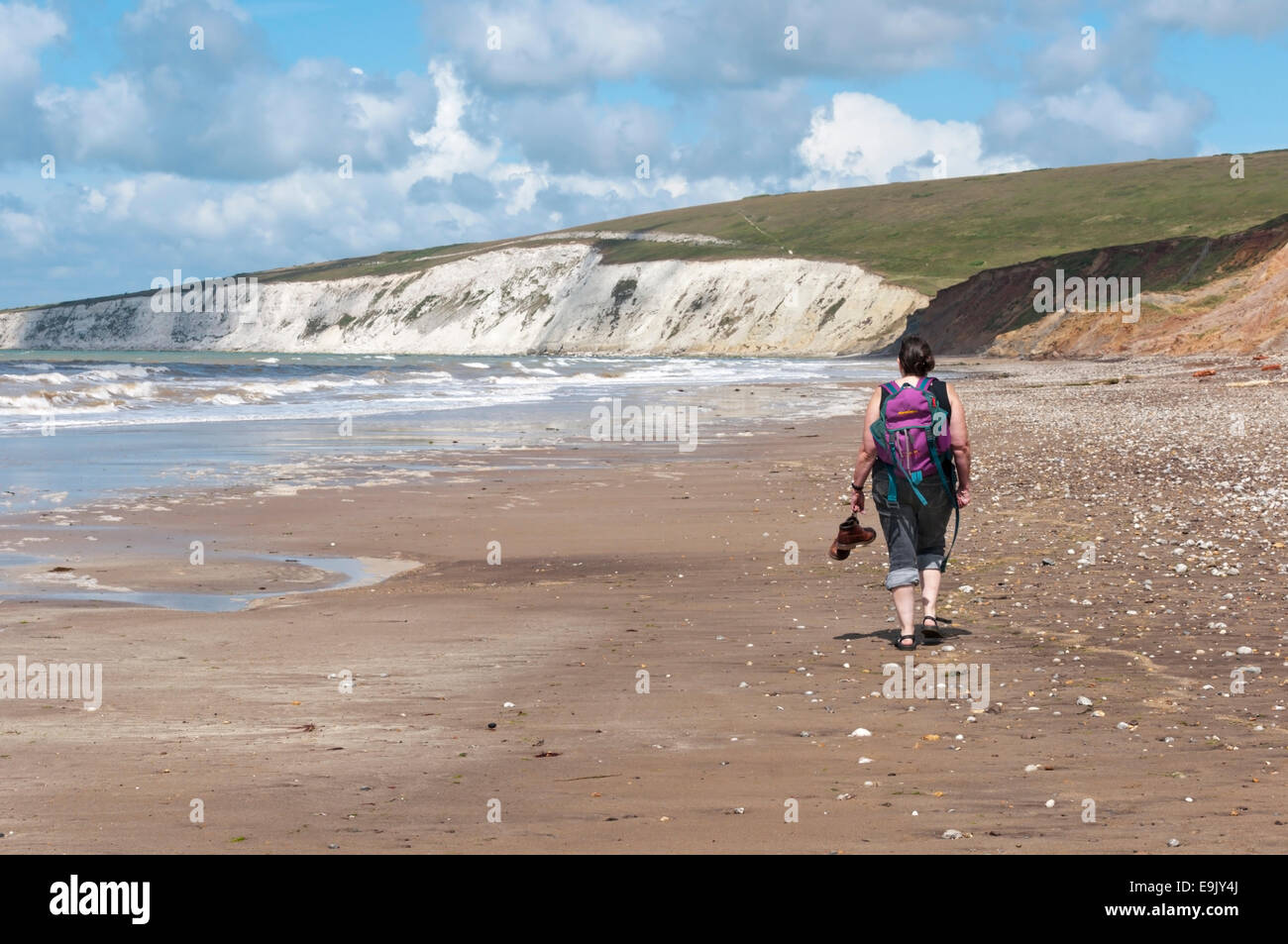 Woman walking, carrying her boots, at Brook Bay - at the southern end of the Hamstead Trail that crosses the Isle of Wight. Stock Photo