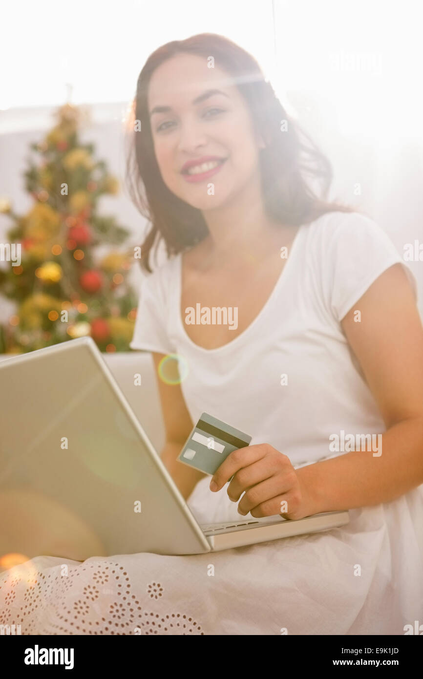 Smiling brunette shopping online with laptop at christmas Stock Photo