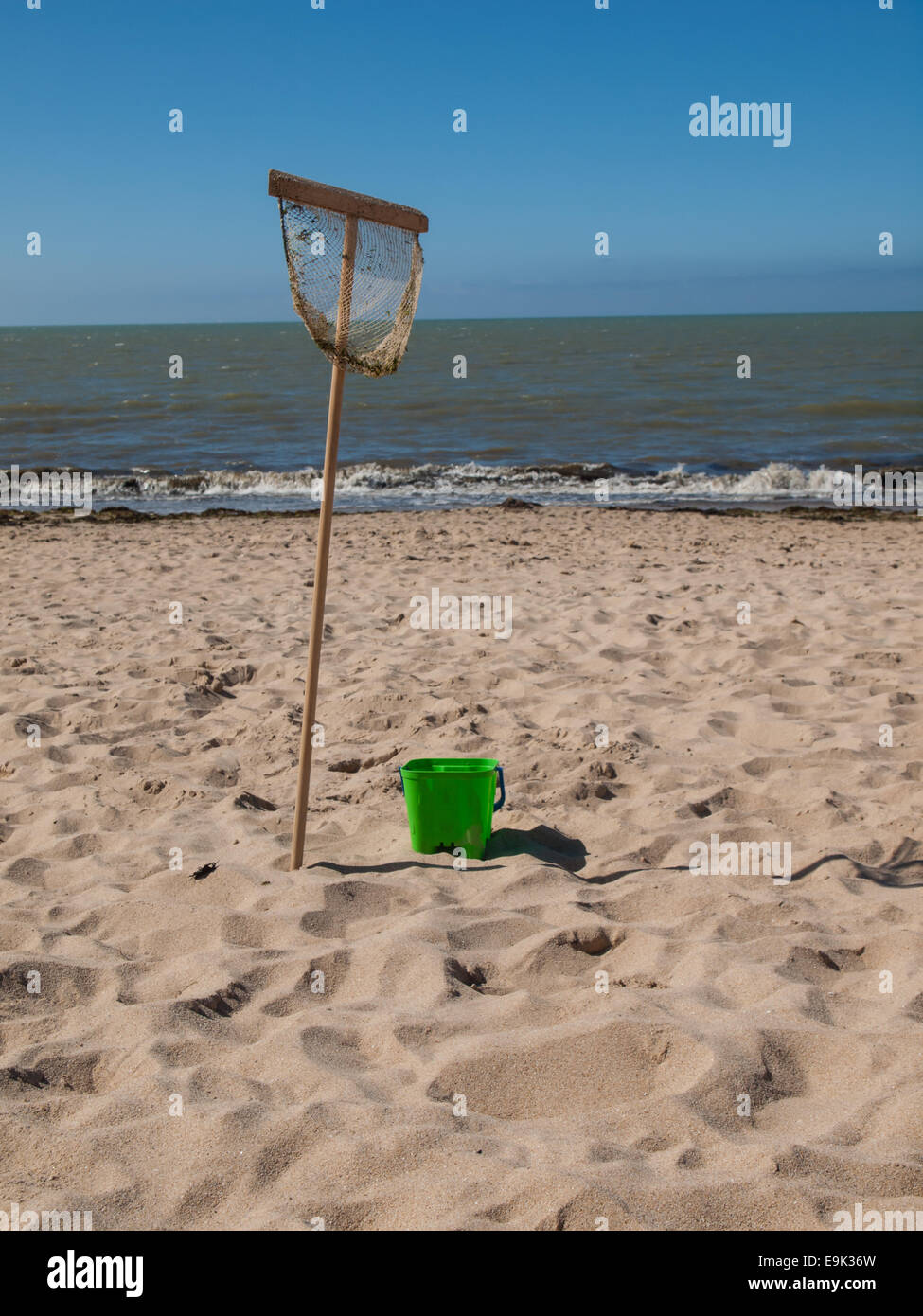 fishing net and bucket on the beach with sea behind on a sunny summer day Stock Photo
