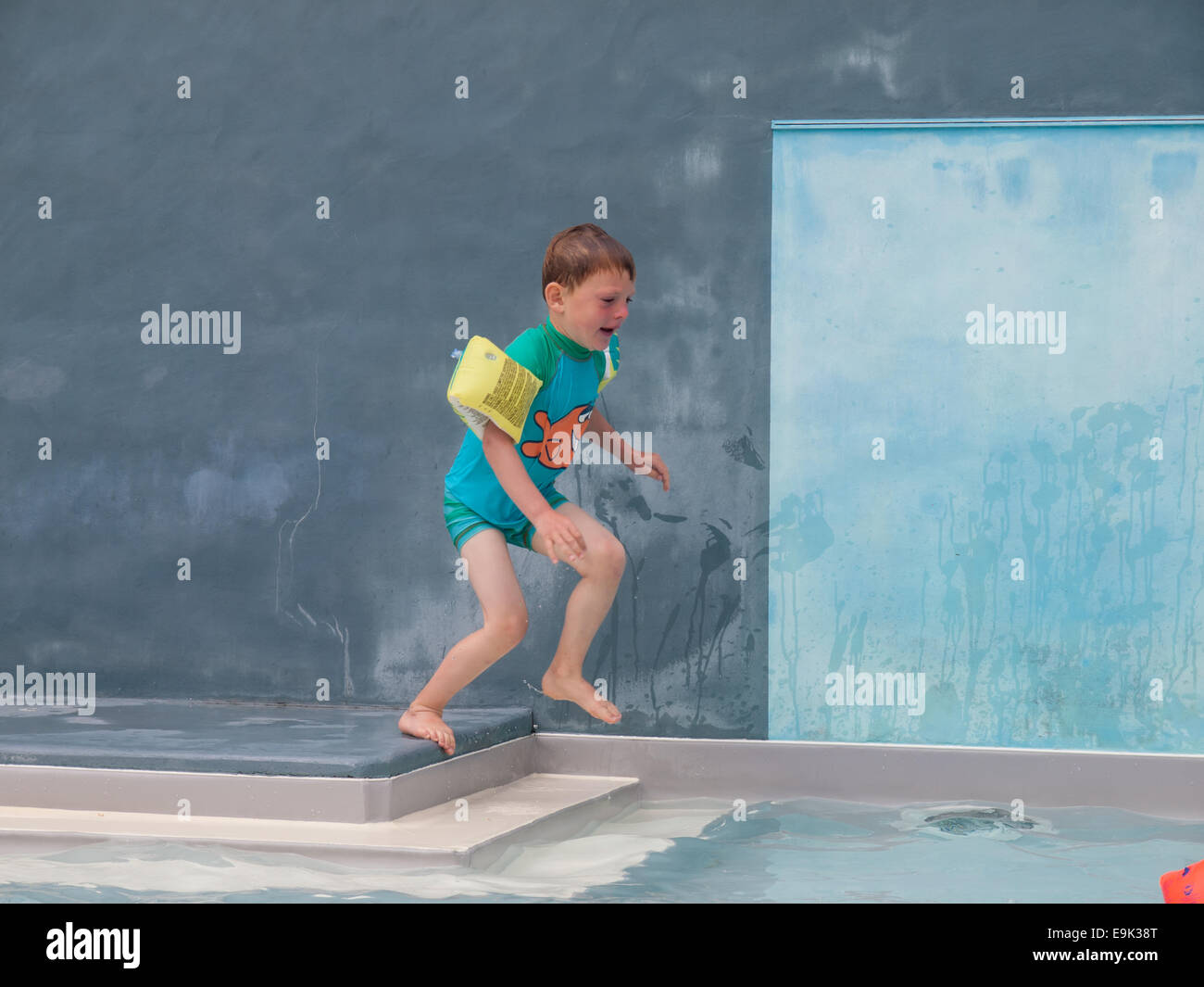 small boy in armbands jumping into an outdoor swimming pool Stock Photo