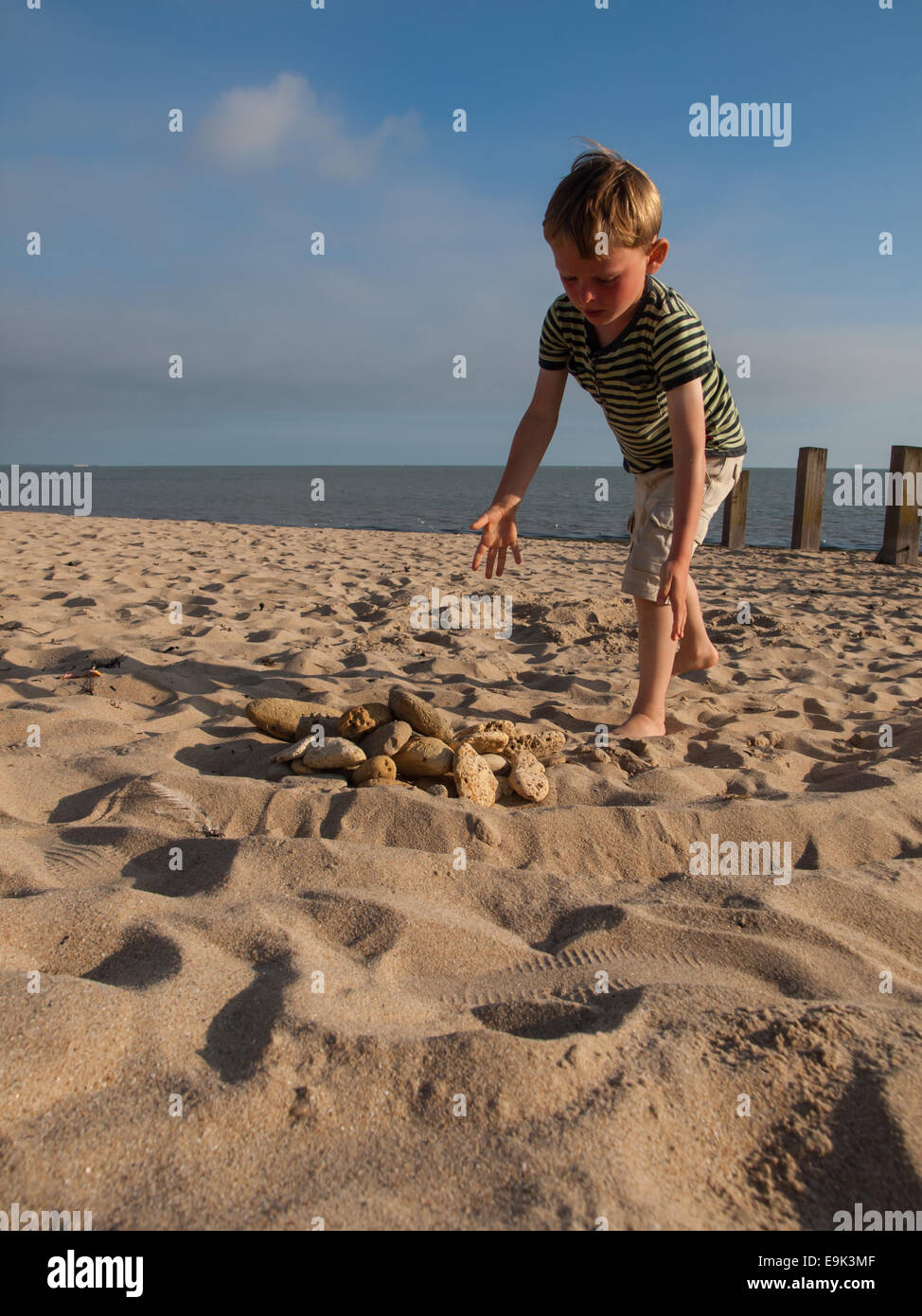 small boy collecting stones on a sandy beach Stock Photo