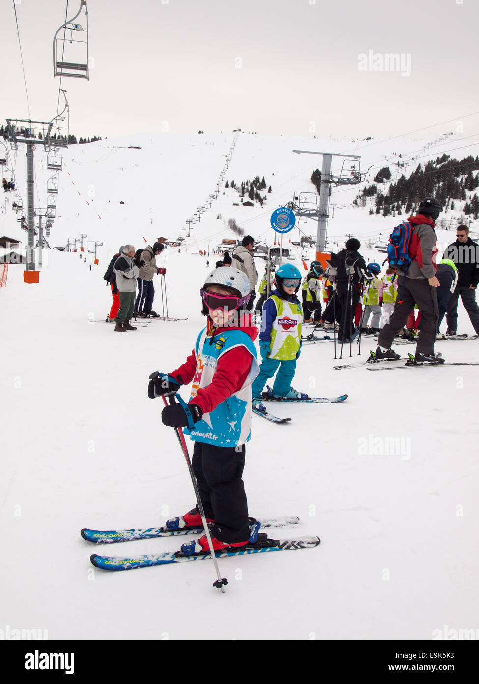 small girl on skis wearing ski clothes and helmet waiting  for a skiing lesson at a ski school collection point Stock Photo