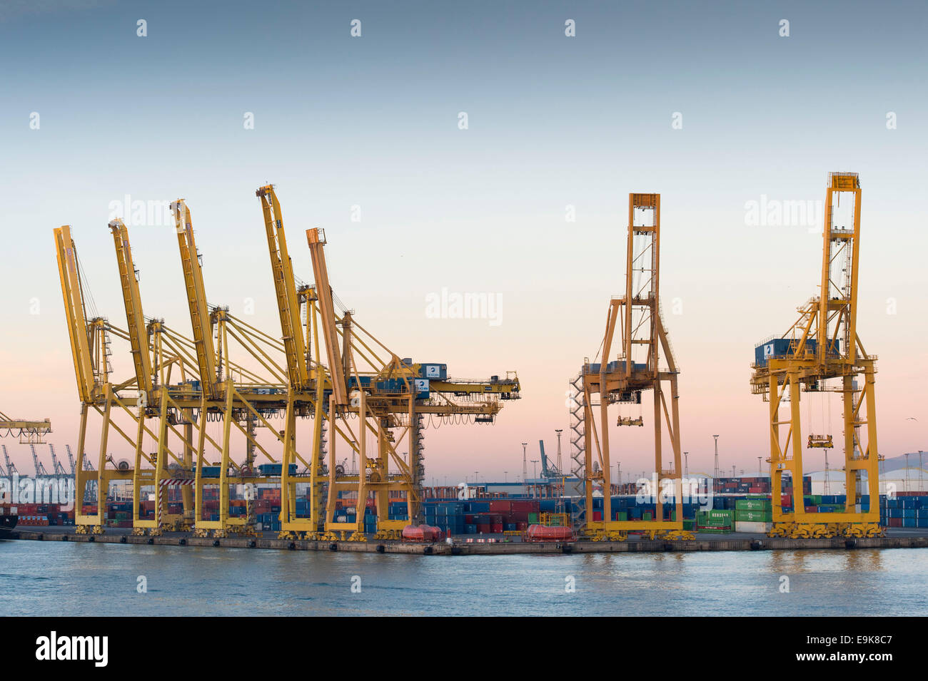 Yellow cranes move shipping containers at Barcelona's main port - Port de Barcelona - at sunrise. Stock Photo