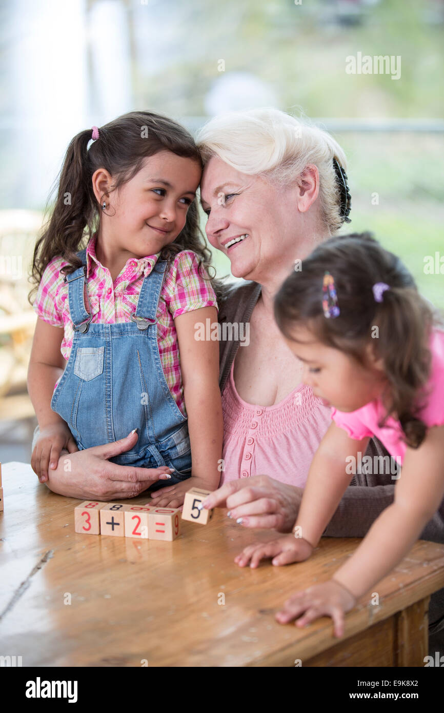 Loving grandmother teaching calculation to granddaughters at table in house Stock Photo