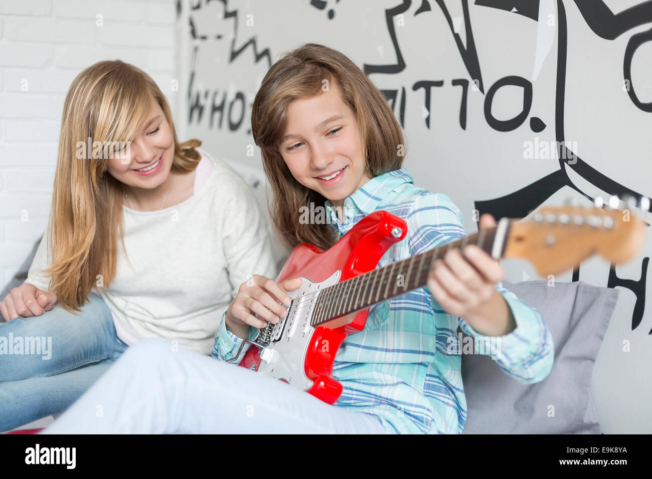 Girl listening to sister playing guitar at home Stock Photo