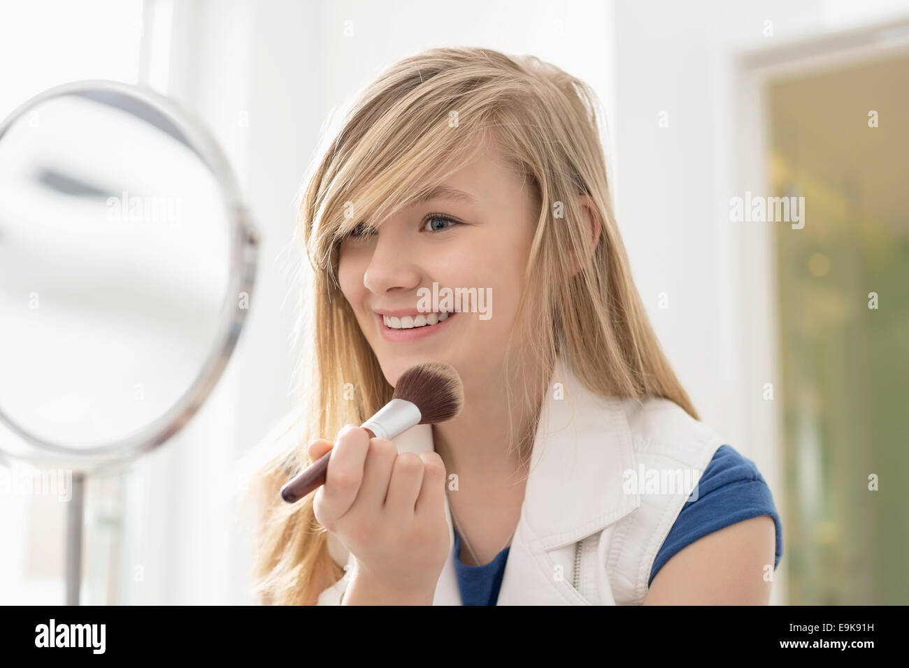 Girl applying makeup in front of mirror at home Stock Photo