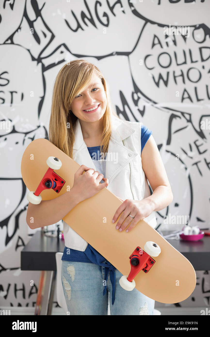 Portrait of happy teenage girl holding skateboard at home Stock Photo