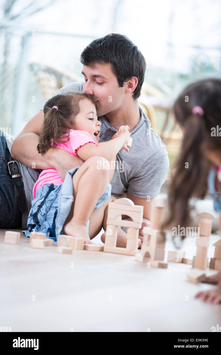 Loving father kissing daughter building blocks on floor Stock Photo