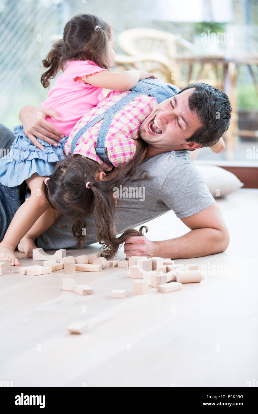 Playful daughters on top of father at home Stock Photo