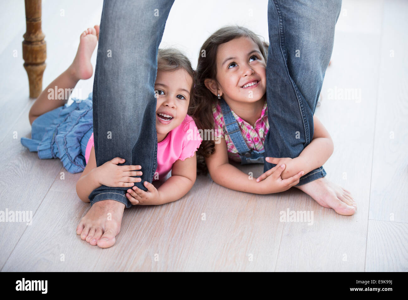 Playful girls holding father's legs on hardwood floor Stock Photo