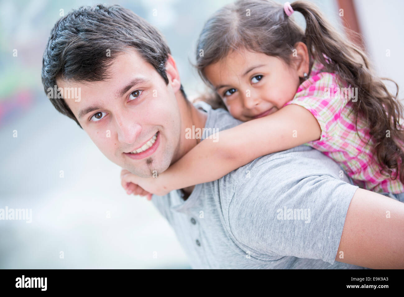 Side view portrait of smiling man piggybacking little daughter at home Stock Photo