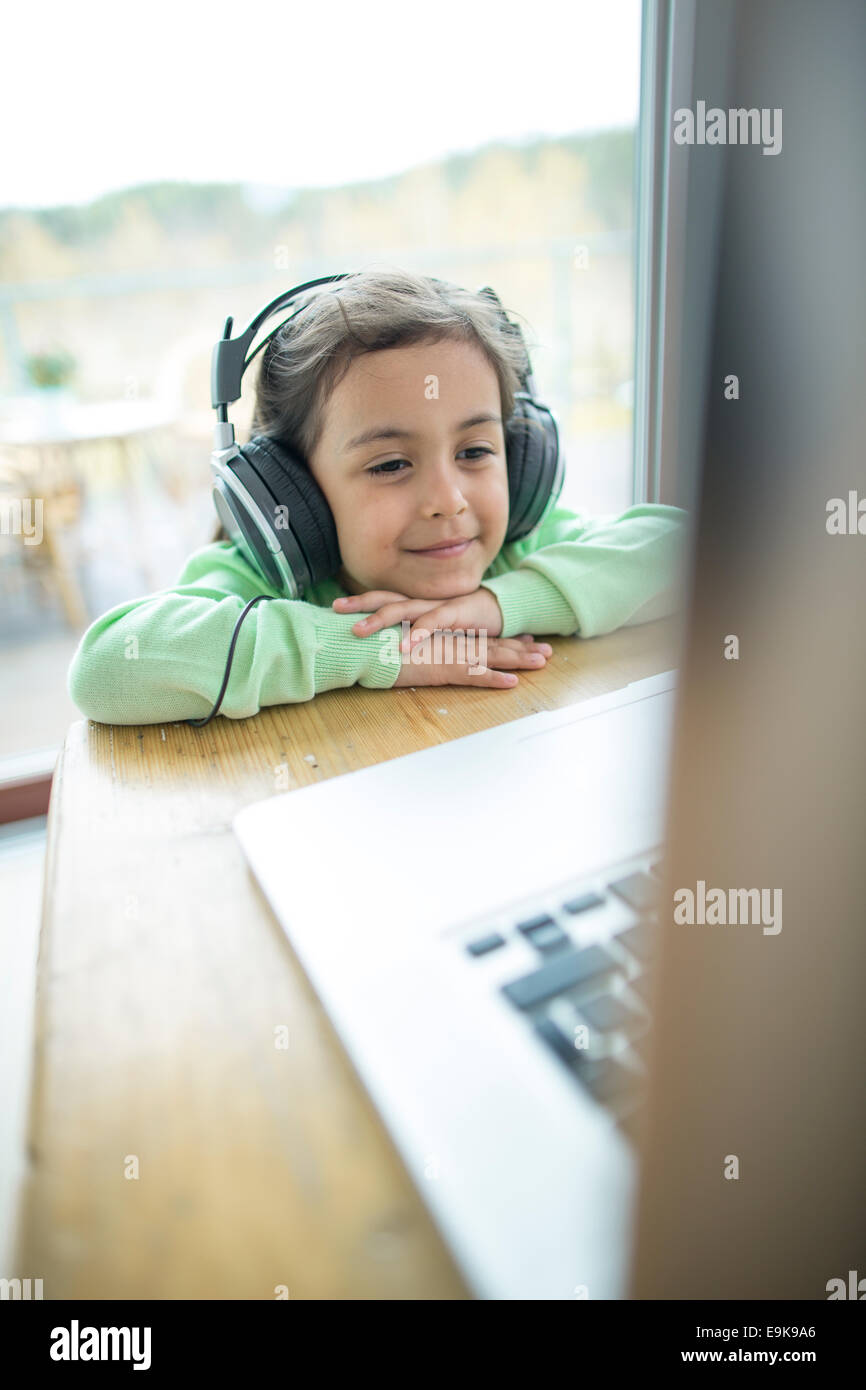 Cute little girl listening to music on headphones while using laptop at ...