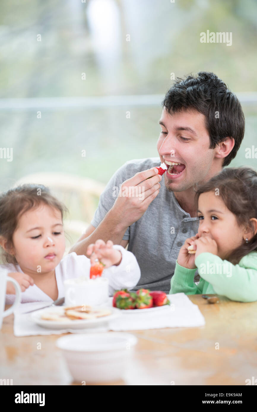 Father and daughters eating strawberries with whipped cream at home Stock Photo