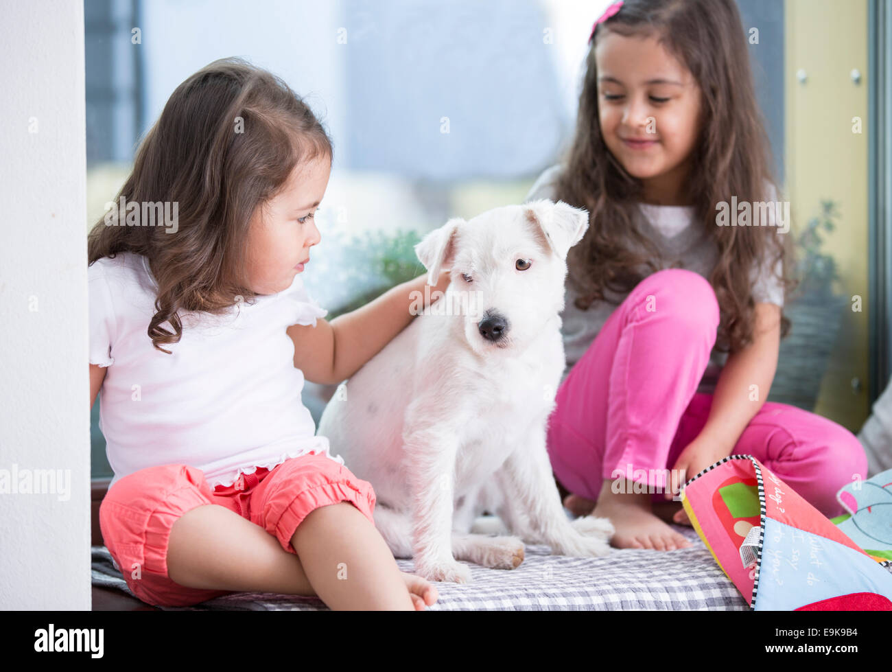 Cute girls with puppy sitting on bed Stock Photo