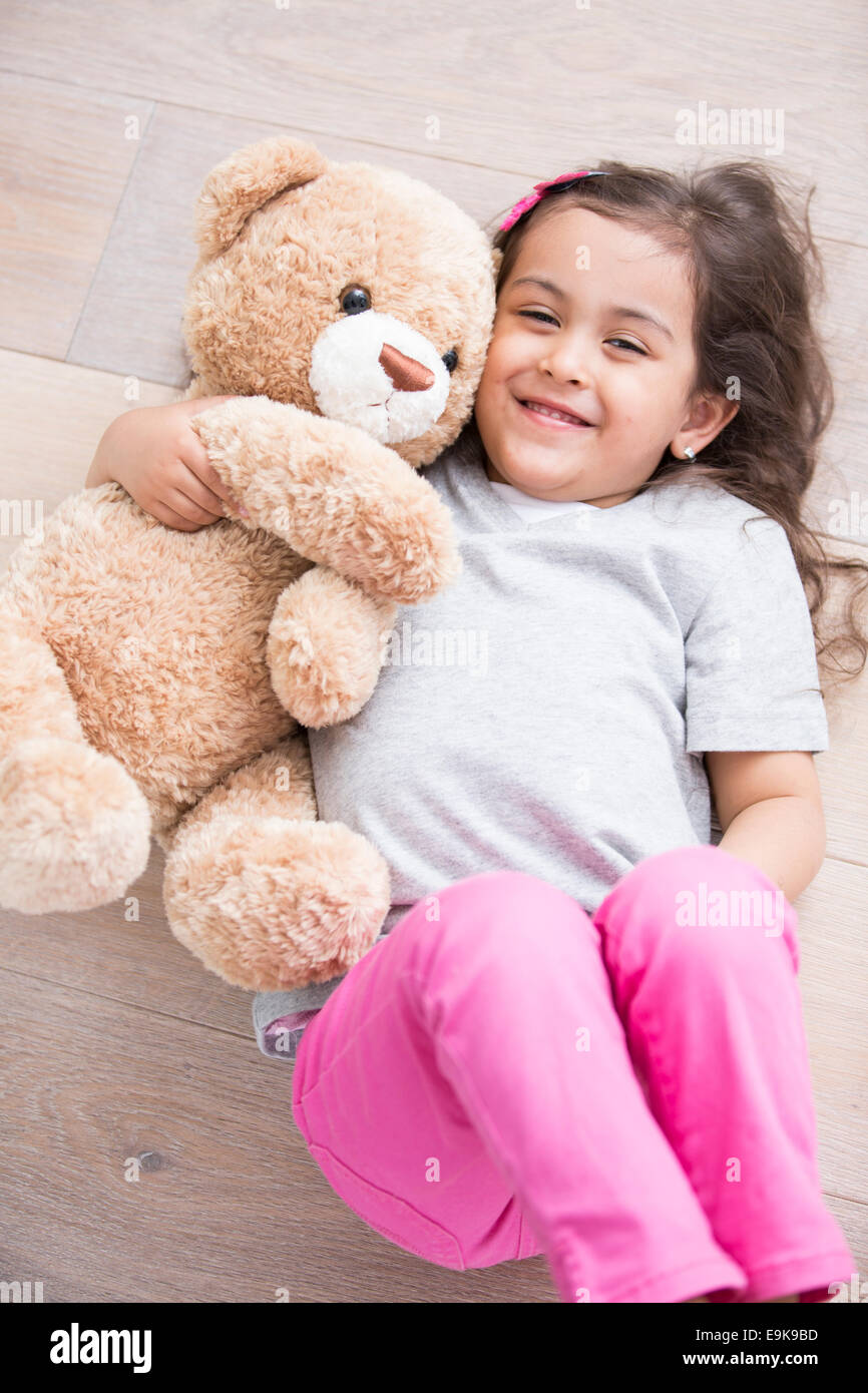 Happy girl with teddy bear lying on wooden floor at home Stock Photo ...