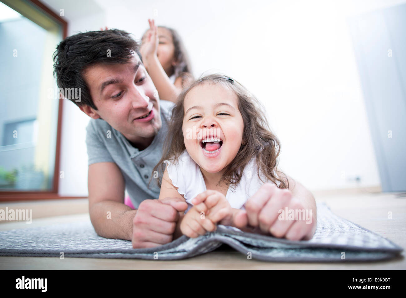 Father looking at cheerful daughter lying on blanket at home Stock Photo