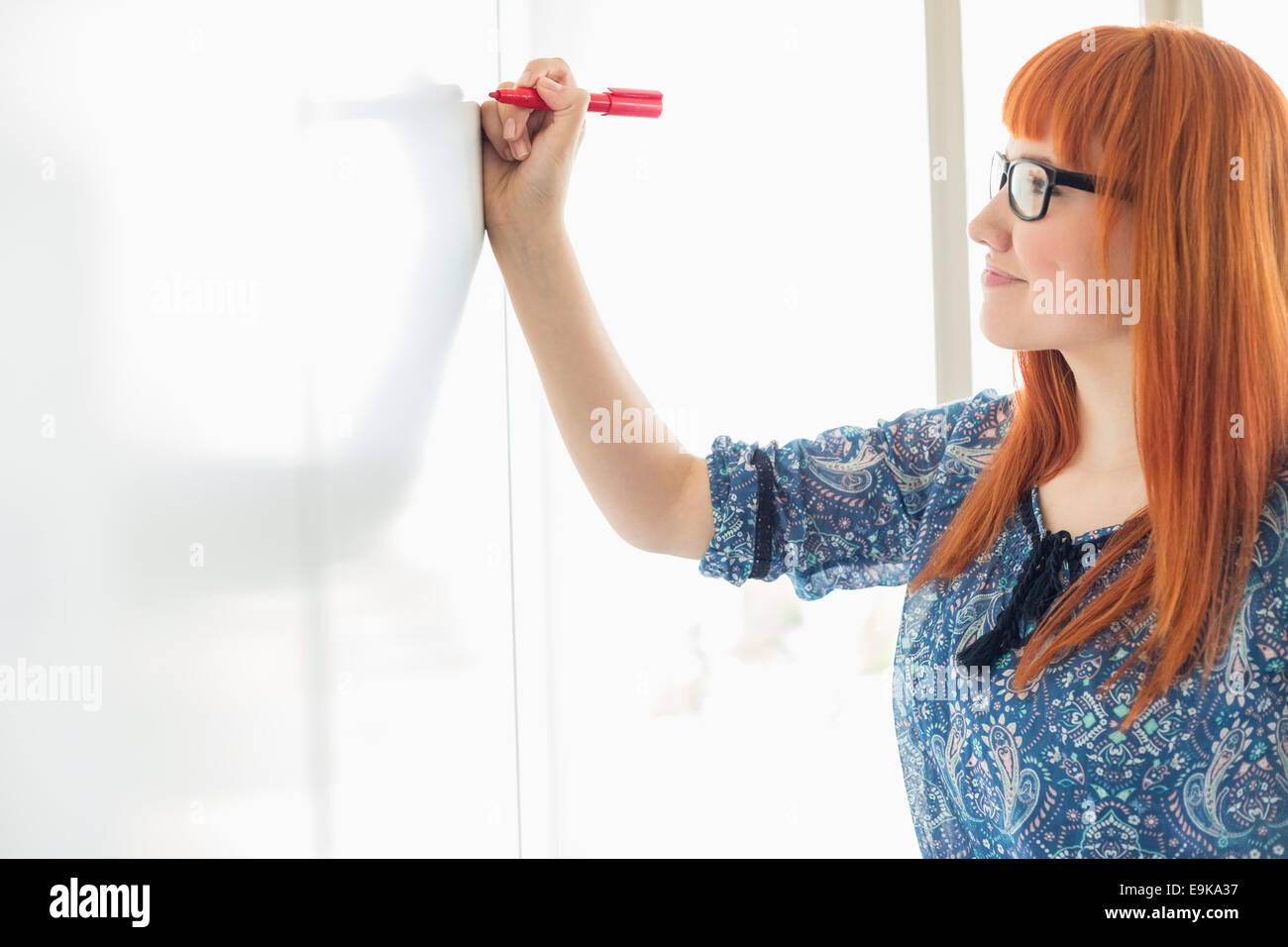 Smiling businesswomen writing on whiteboard in creative office Stock Photo