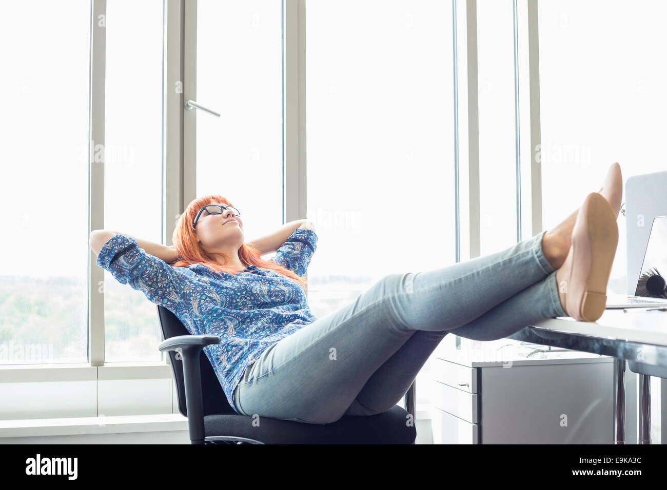 Full-length of businesswoman relaxing with feet up at desk in creative office Stock Photo