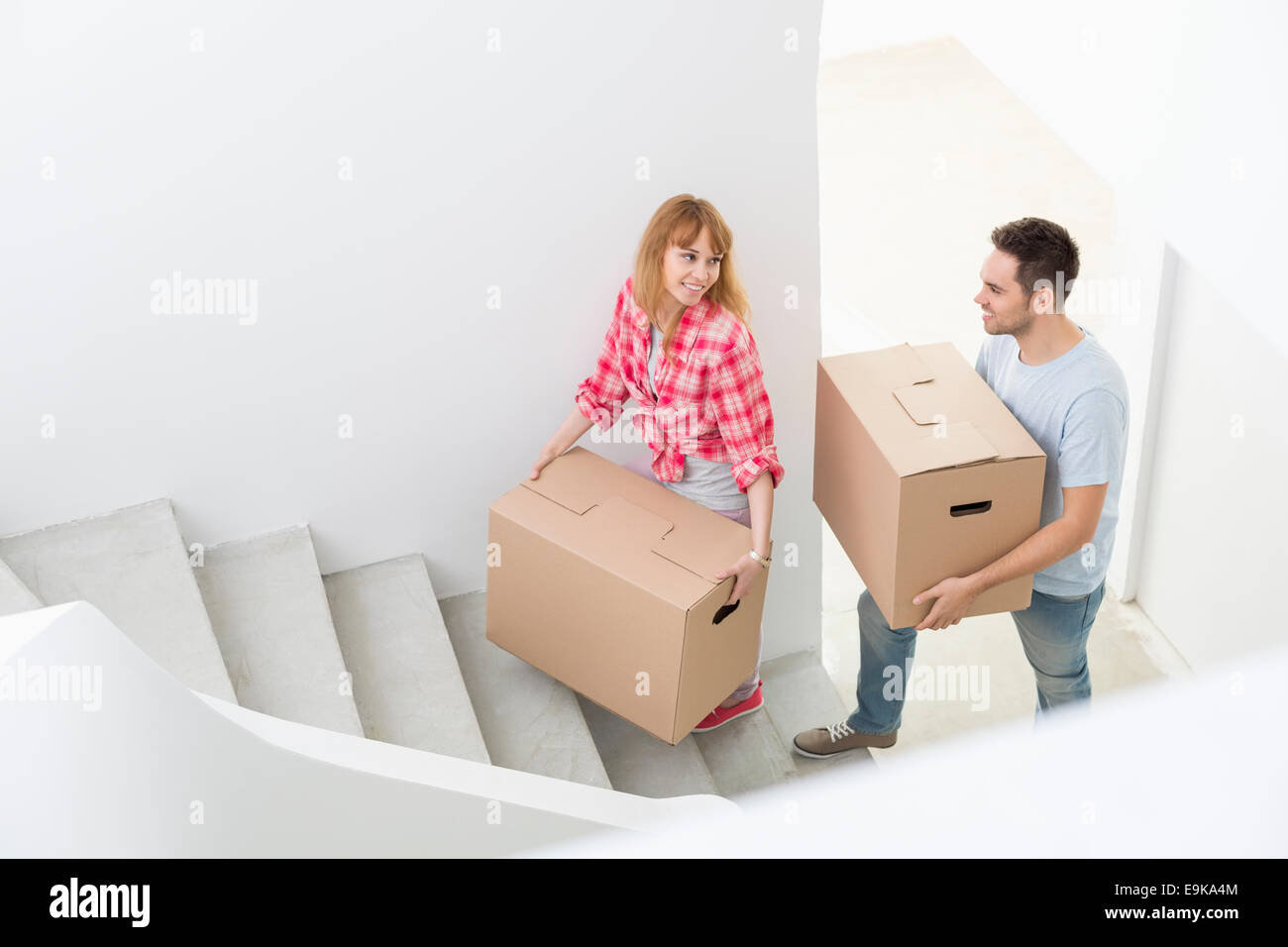 Happy couple carrying moving boxes up stairs in new house Stock Photo