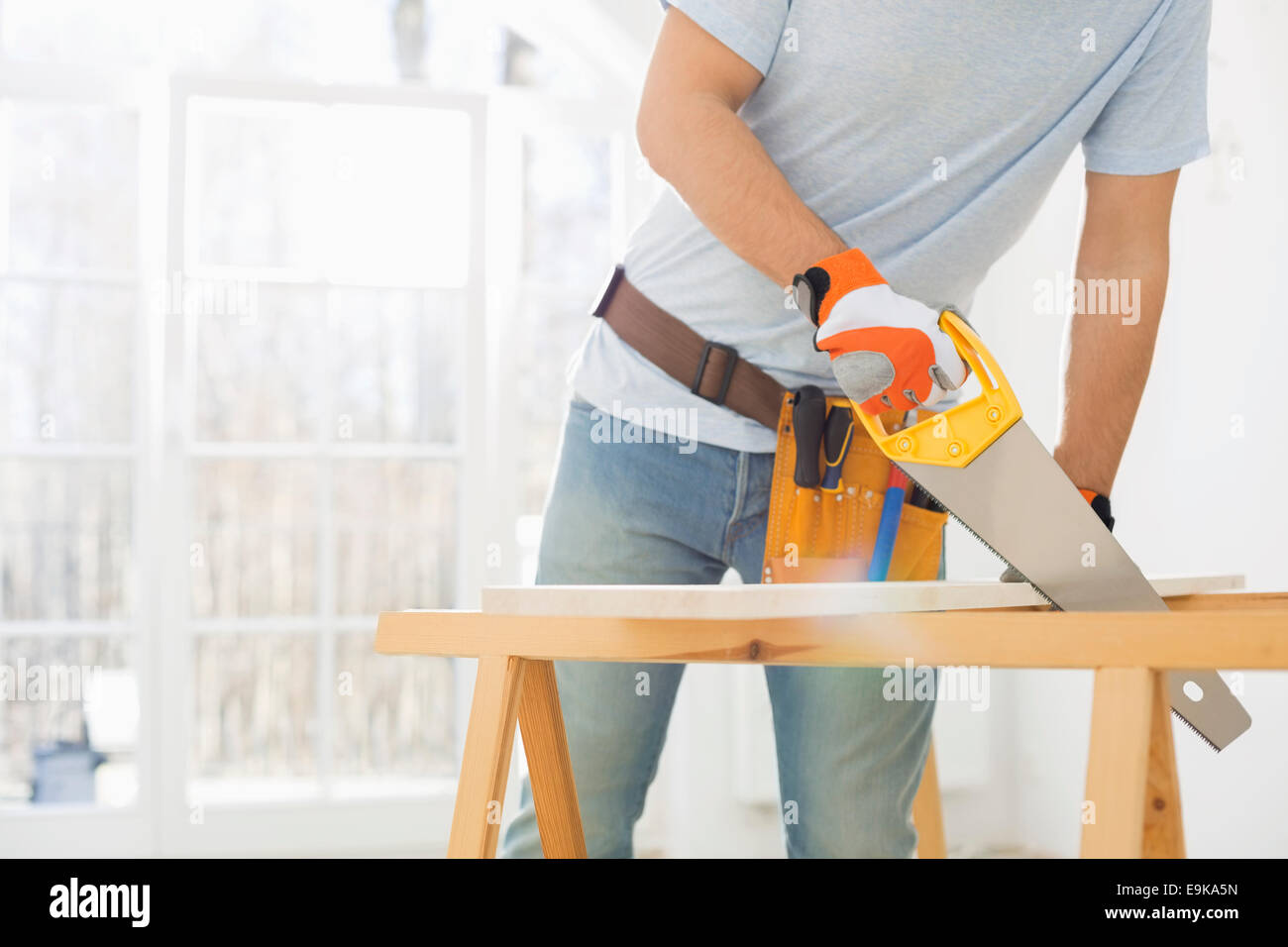 Midsection of man sawing wood in new house Stock Photo