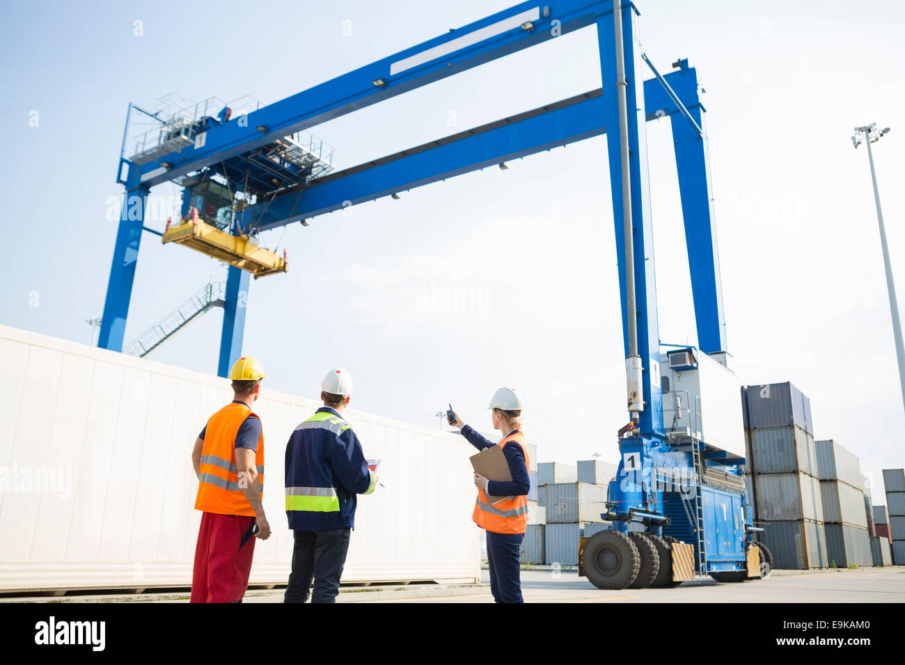 Workers discussing against large crane loading container at shipping yard Stock Photo