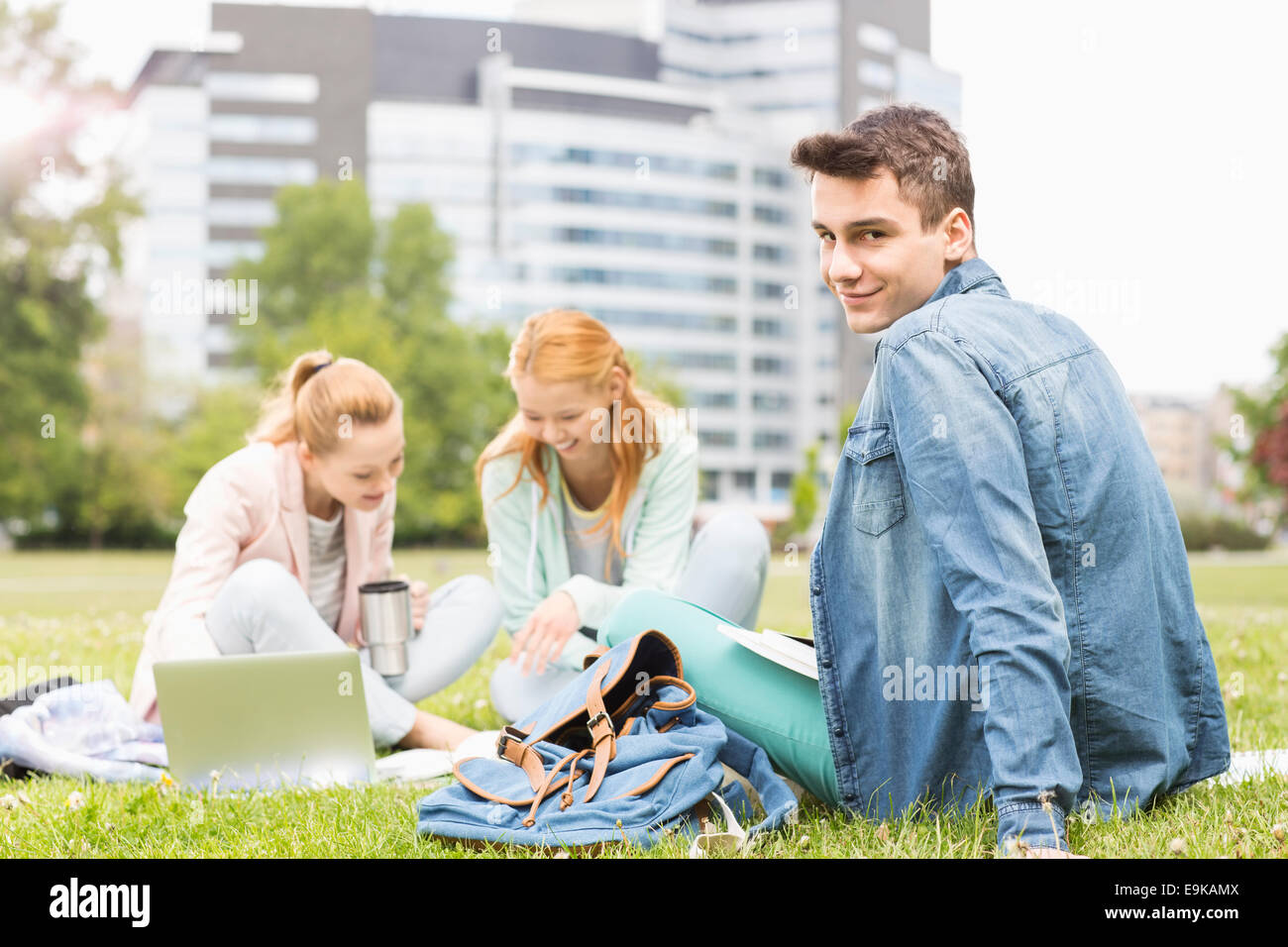 Portrait of young man with female friends studying on university campus ...