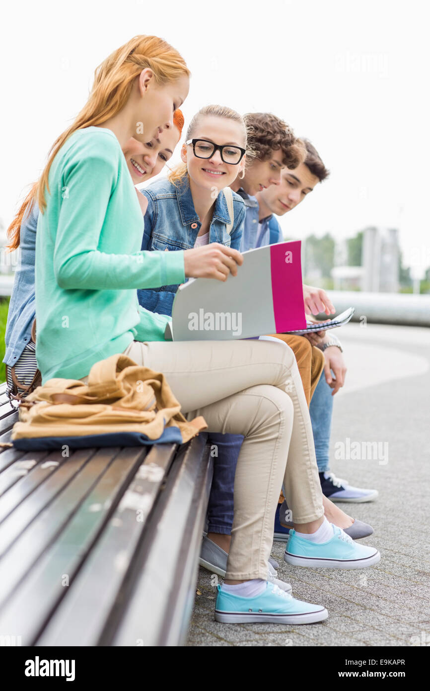University students studying while sitting on low wall in park Stock Photo