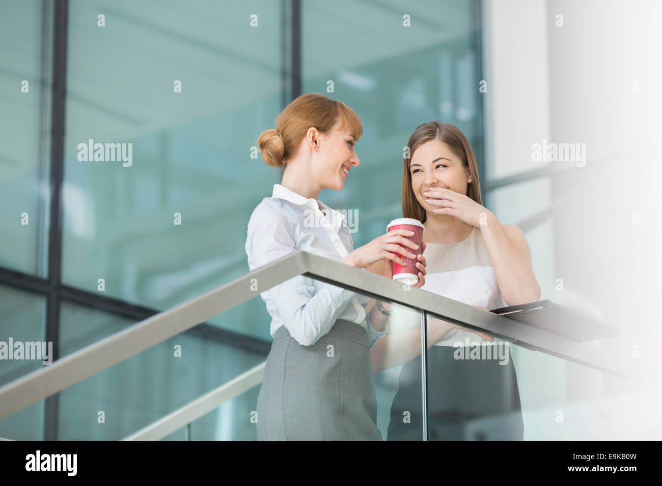 Businesswomen gossiping while having coffee on steps in office Stock Photo