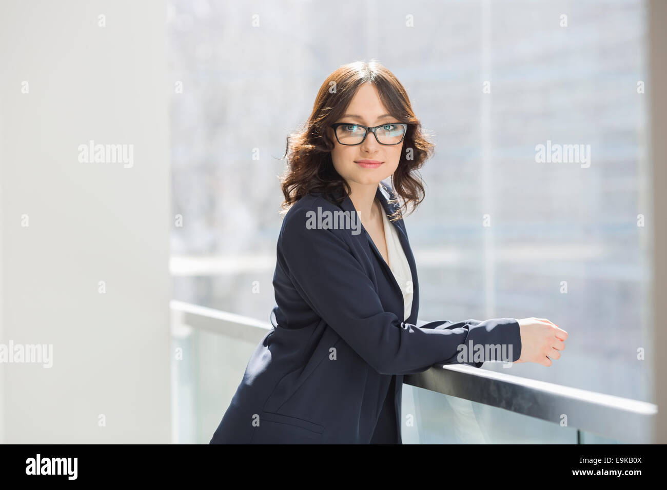 Portrait of confident young businesswoman leaning on railing in office ...