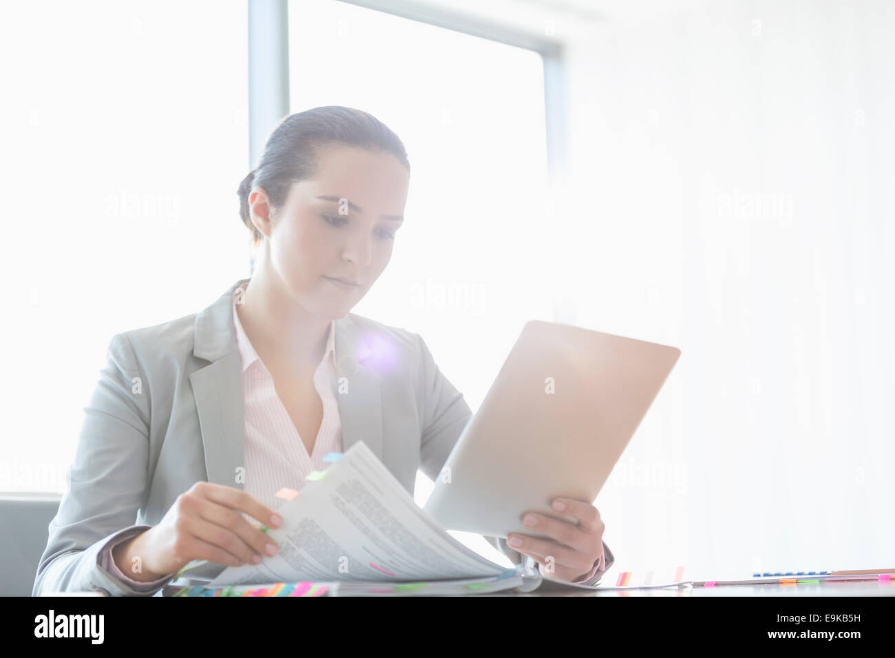Young businesswoman using tablet PC while reading book in office Stock Photo