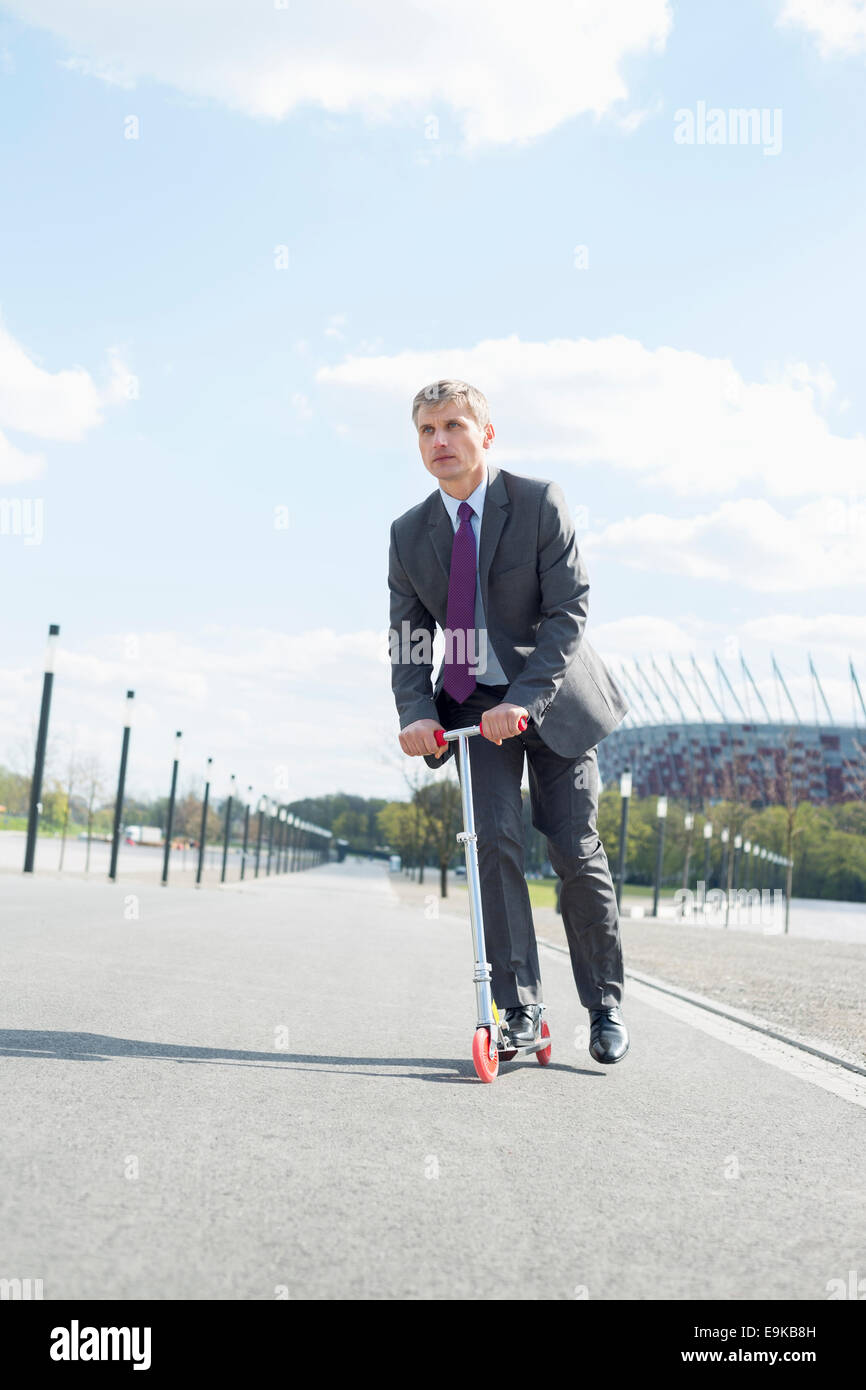 Businessman looking away while riding scooter on street Stock Photo