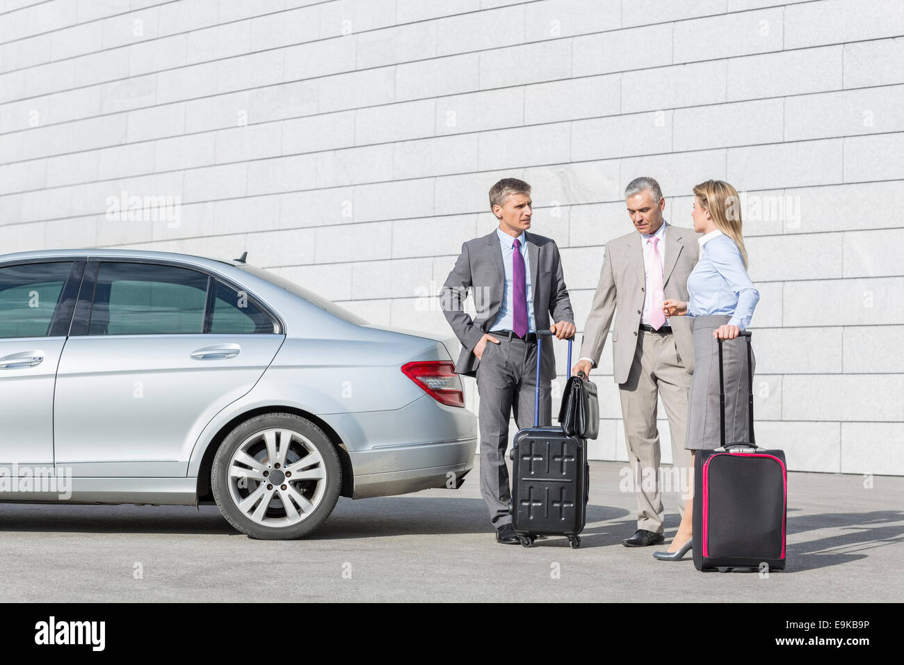 Businesspeople with luggage discussing outside car on street Stock Photo