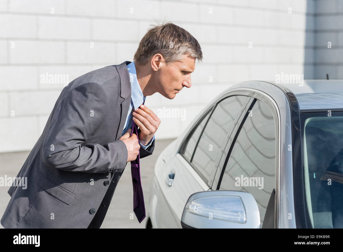 Side View Of Businessman Adjusting Tie While Looking In Car Window side-view-of-businessman-adjusting-tie-while-looking-in-car-window