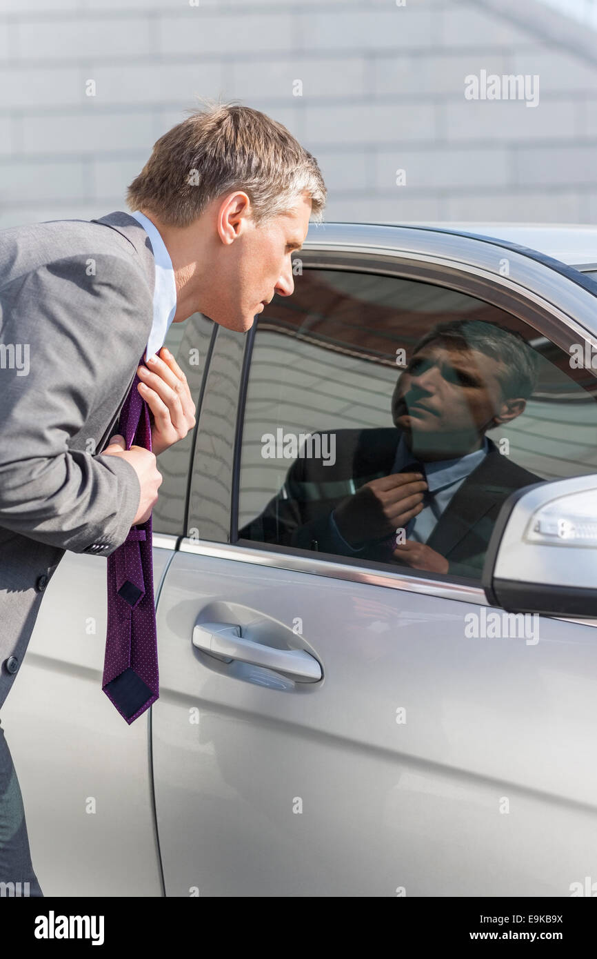 Businessman adjusting tie while looking in car window Stock Photo