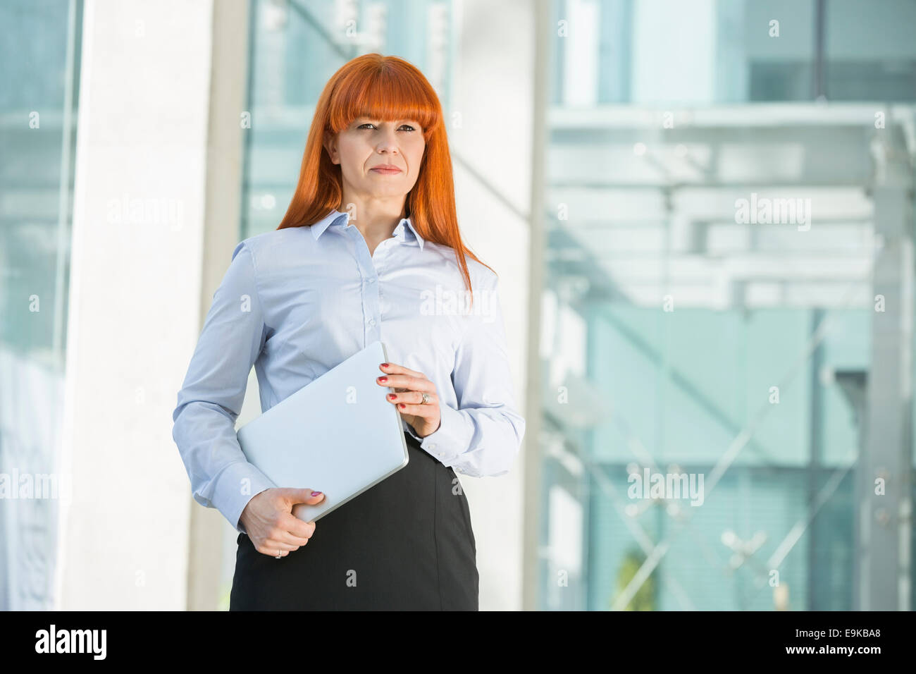 Confident businesswoman looking away while holding laptop in office Stock Photo