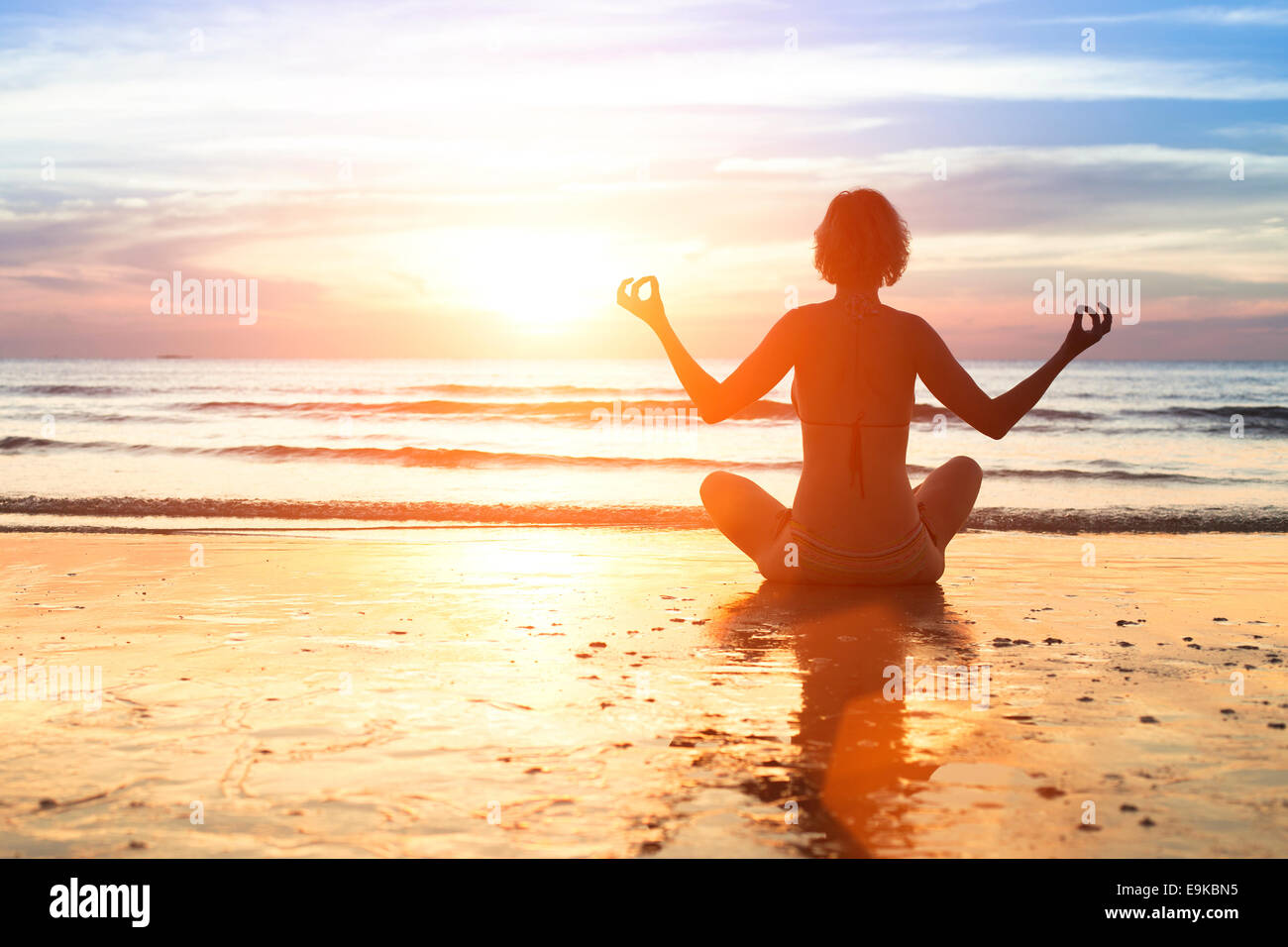 Yoga woman in the lotus position sitting on a sea beach during sunset ...