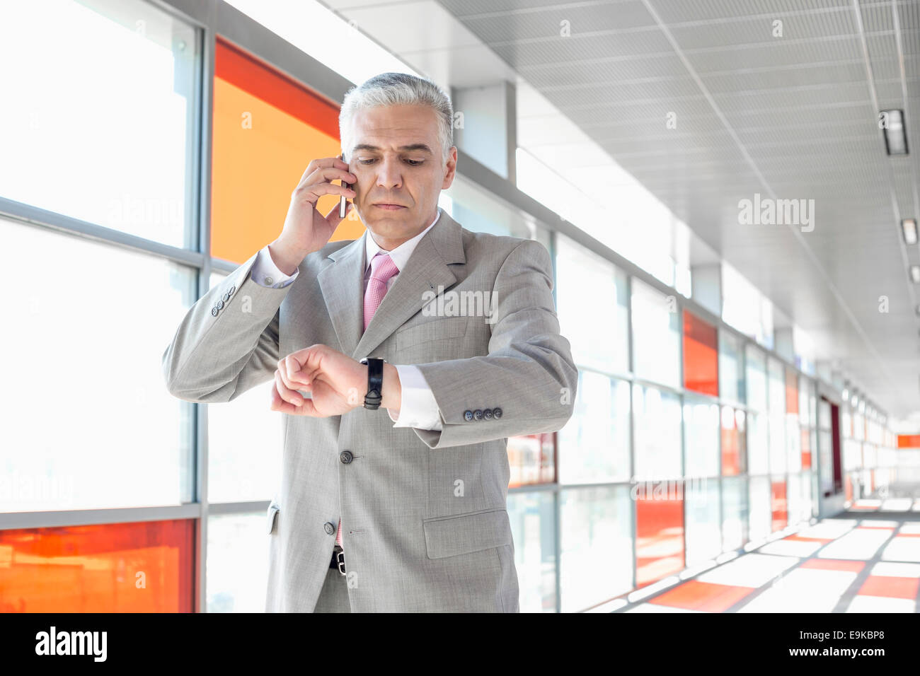 Middle aged businessman checking time while on call at railroad station ...