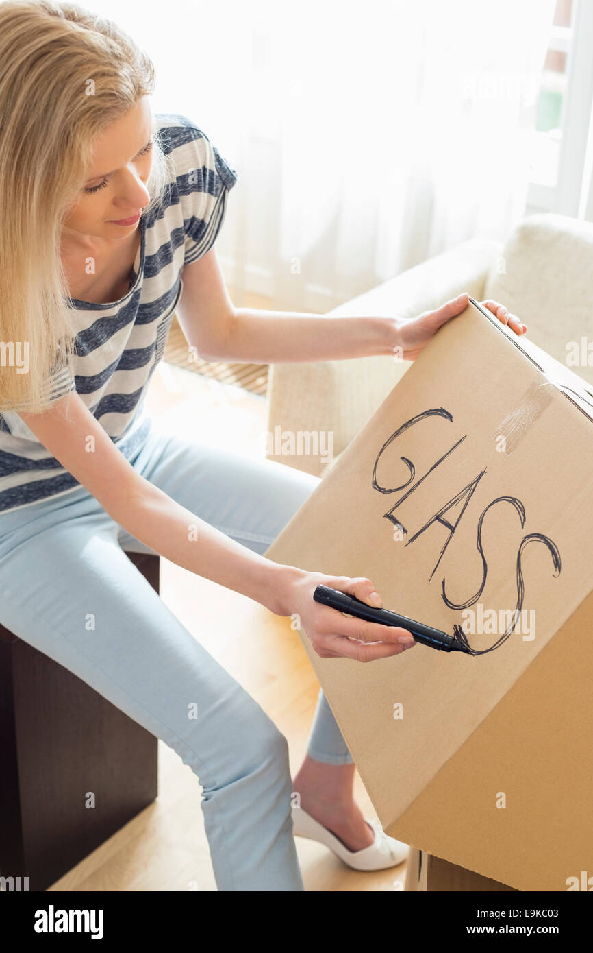 Woman labeling moving box with glass material at home Stock Photo