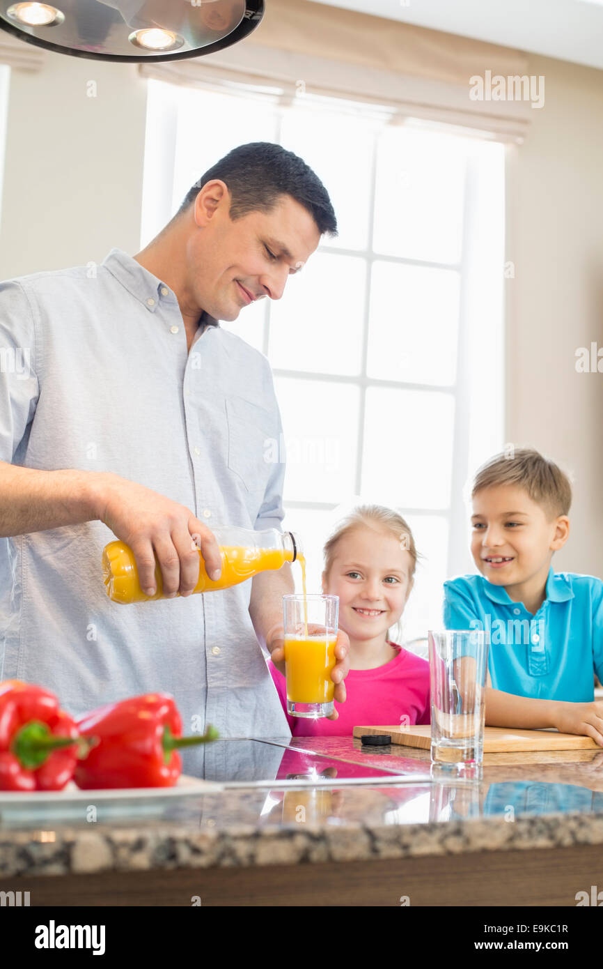 Father serving orange juice for children in kitchen Stock Photo Alamy