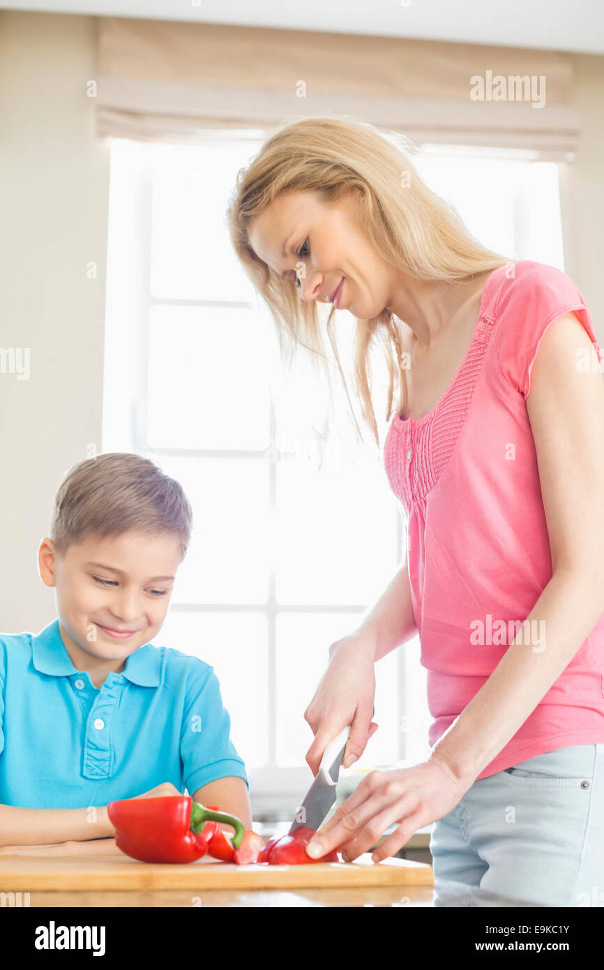 Boy looking at mother slicing red bell pepper in kitchen Stock Photo