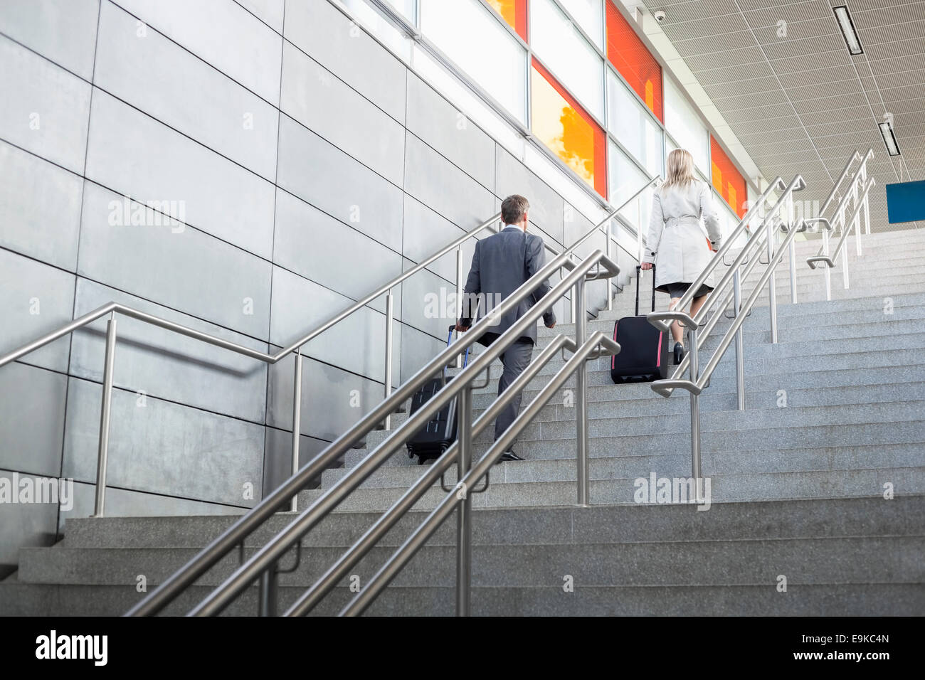 Rear view of businessman and businesswoman with luggage moving upstairs in railroad station Stock Photo