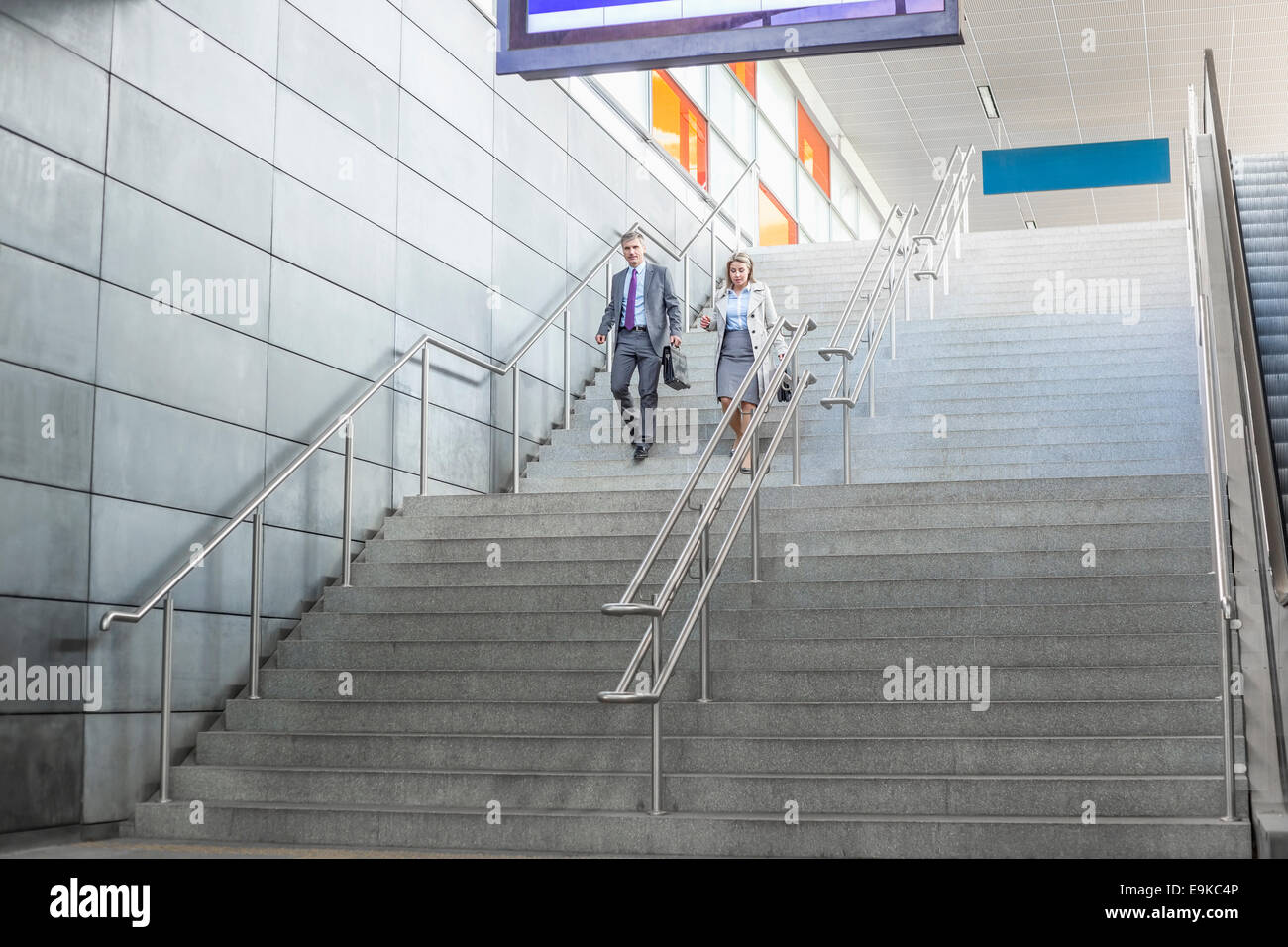 Full length of businessman and businesswoman walk down stairs at railway station Stock Photo