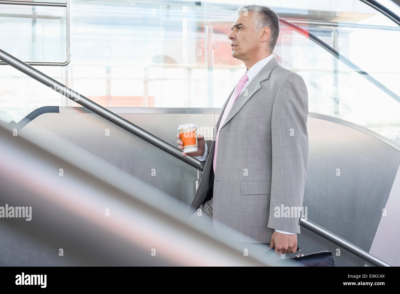 Side view of middle aged businessman with coffee cup walking up stairs in railroad station Stock Photo