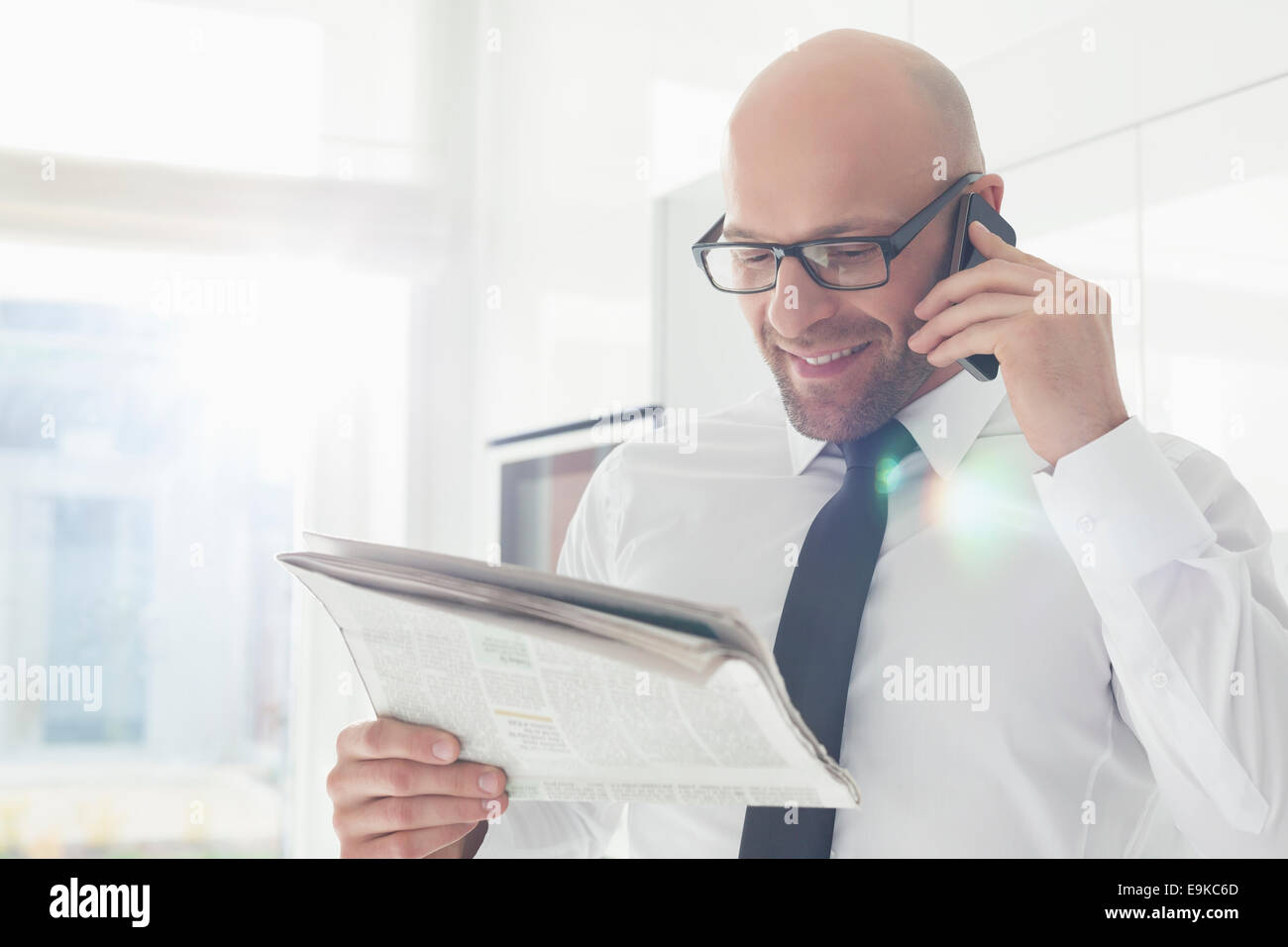 Happy businessman on call while reading newspaper at home Stock Photo