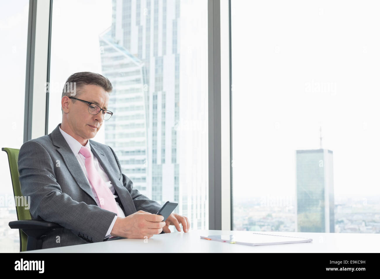 Mature businessman text messaging through cell phone near office window Stock Photo
