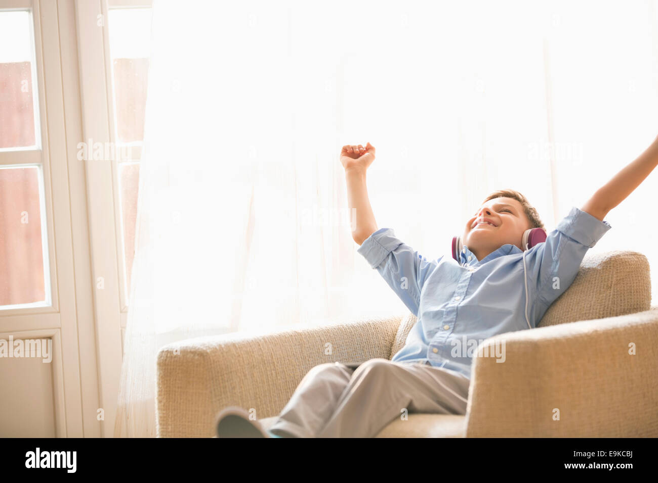 Happy boy with arms raised enjoying music while relaxing on armchair at home Stock Photo