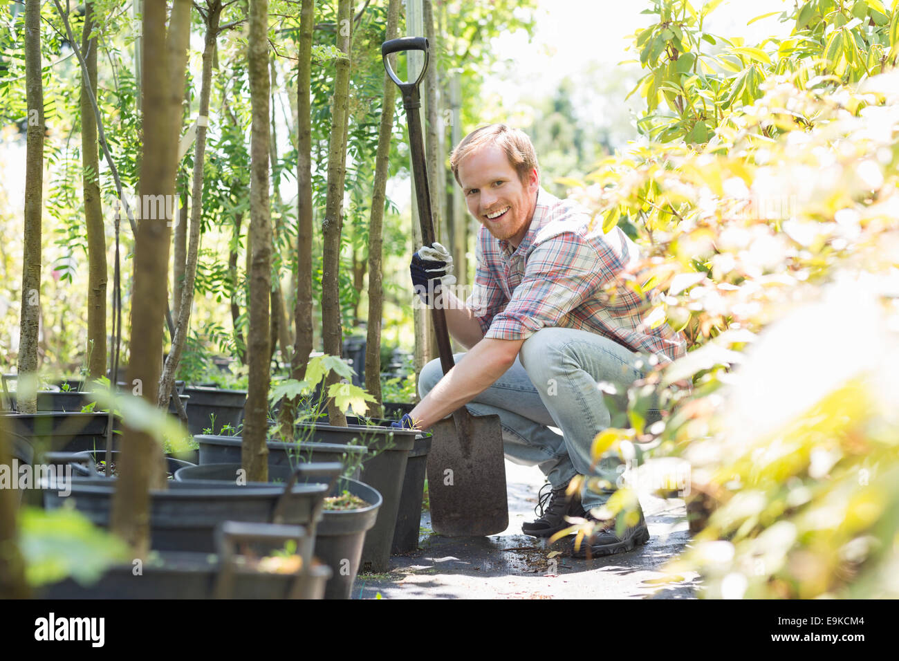 Portrait of happy gardener crouching while holding shovel at plant nursery Stock Photo