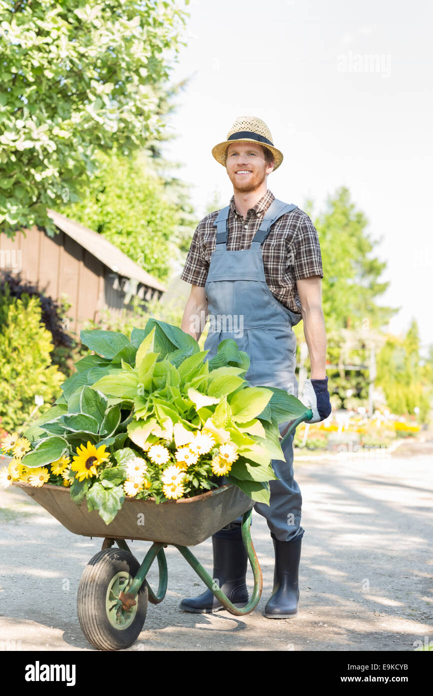 Full length of gardener pushing wheelbarrow with plants at garden