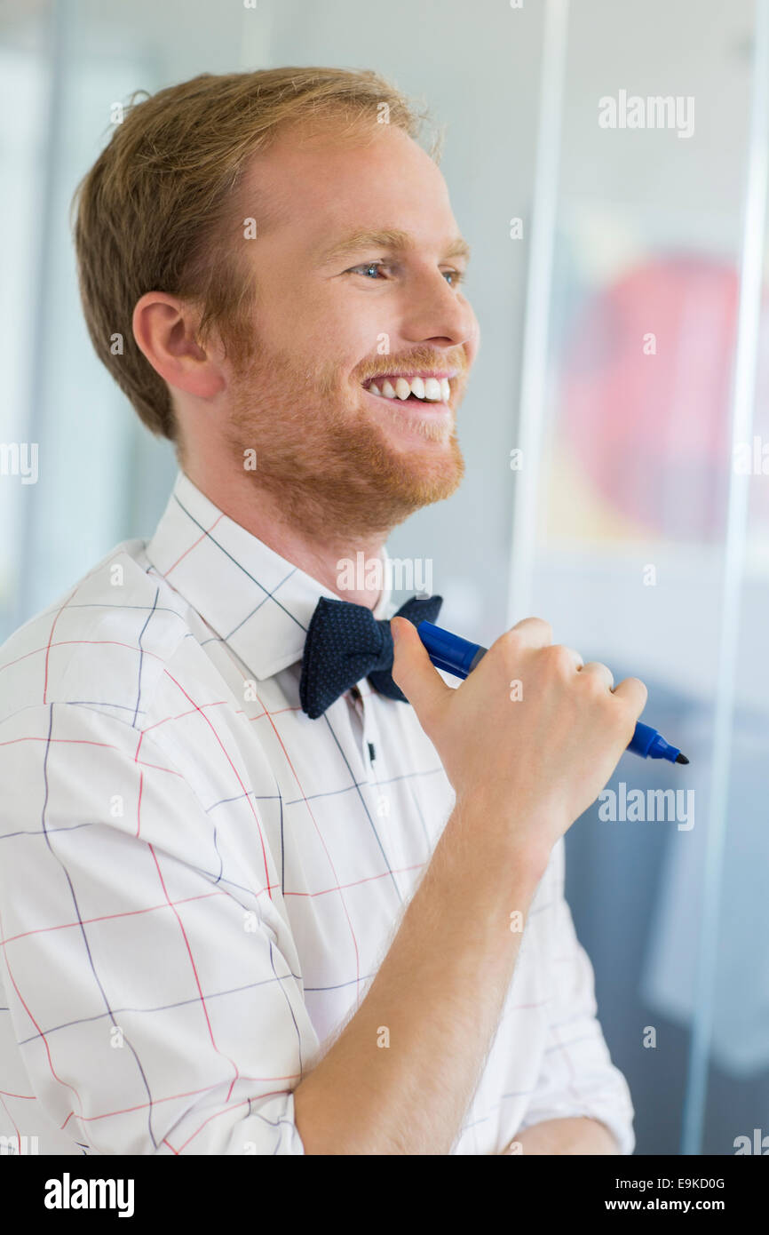 Happy businessman looking away while holding felt tip pen at creative office Stock Photo