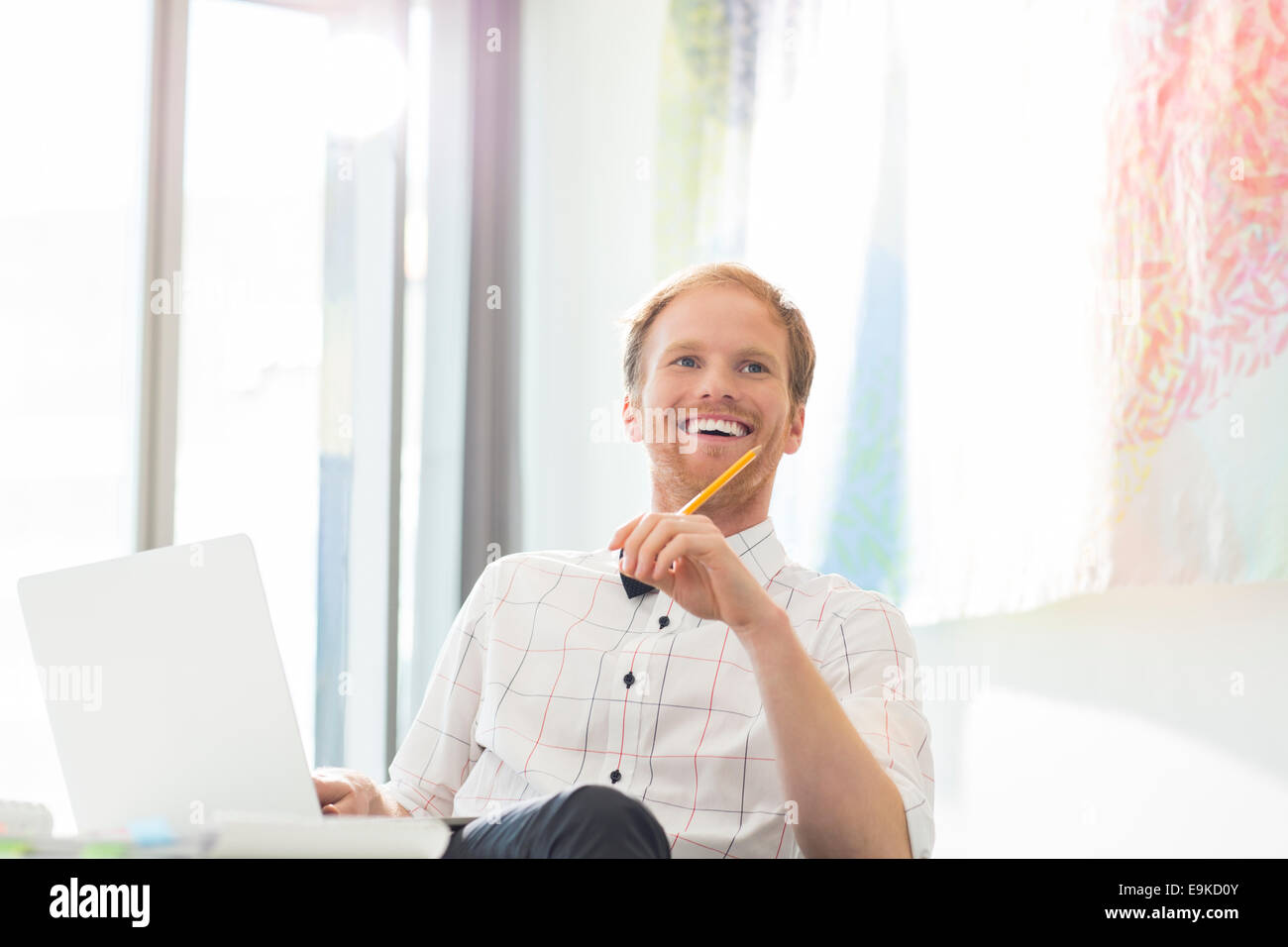 Happy businessman looking away while sitting at desk in creative office Stock Photo